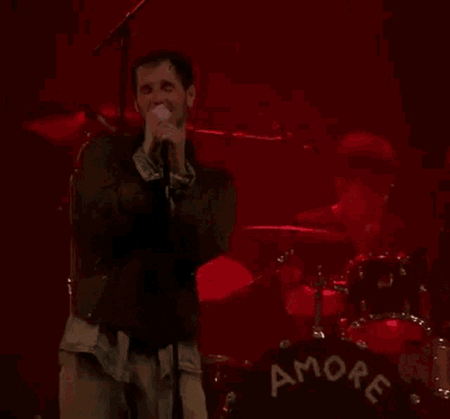 a man singing into a microphone in front of a drum set that says amore on it