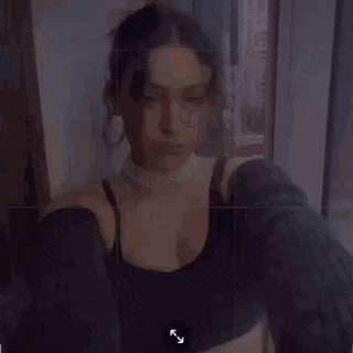 a woman wearing a choker and a sweater is taking a selfie with a camera .