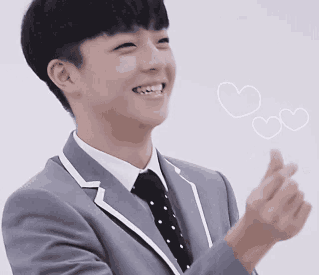 a young man in a suit and tie is smiling and making a heart with his hand