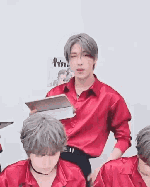 a man in a red shirt is holding a book while standing next to another man .