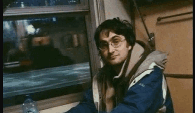 a man in a blue jacket is sitting in front of a window holding a bottle of water