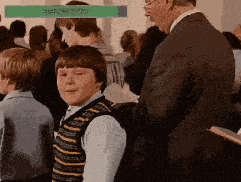 a man in a suit is standing next to a boy in a striped vest in a crowd .