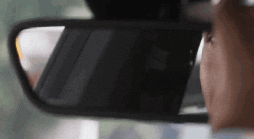a person is looking at their rear view mirror while driving a car