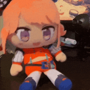 a stuffed doll with orange hair and purple eyes is sitting on a desk .