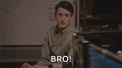 a man in a plaid shirt is sitting at a desk in front of a computer and talking to another man .