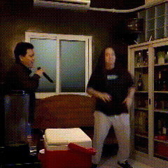 a man is singing into a microphone while another man stands next to a red cooler