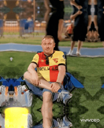a man wearing a shirt that says falk on it sits on a chair