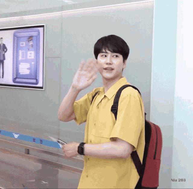a man in a yellow shirt with a red backpack waving
