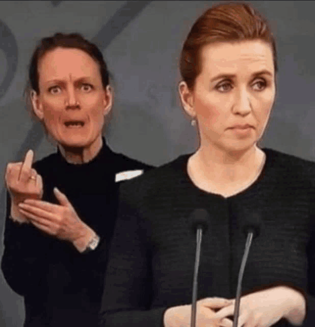 two women are standing next to each other and one is making a funny face while the other is giving a middle finger .
