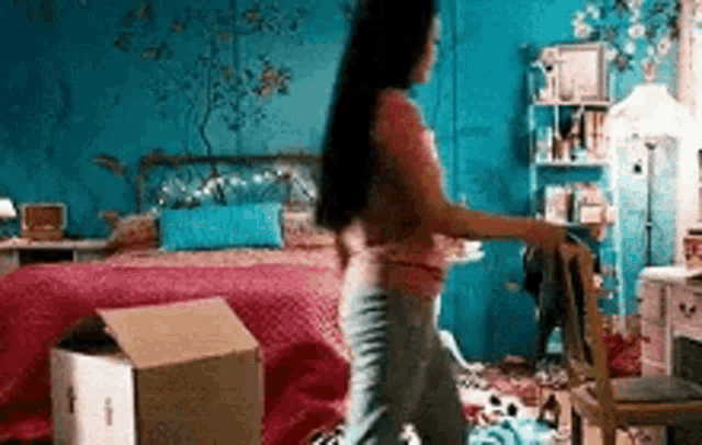 a woman is standing in a messy bedroom with boxes and a bed .