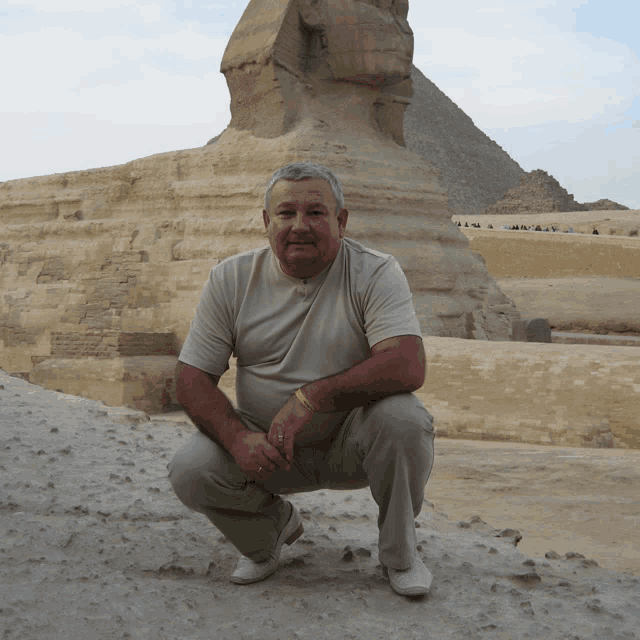 a man squatting in front of a pyramid and statue