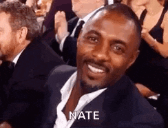 a man in a suit and tie is smiling and sitting in a crowd .