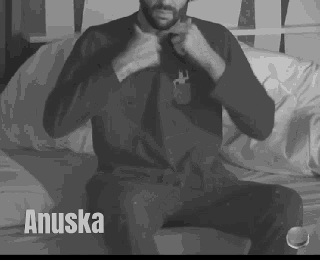 a man is sitting on a bed and the name anuska is on the bottom