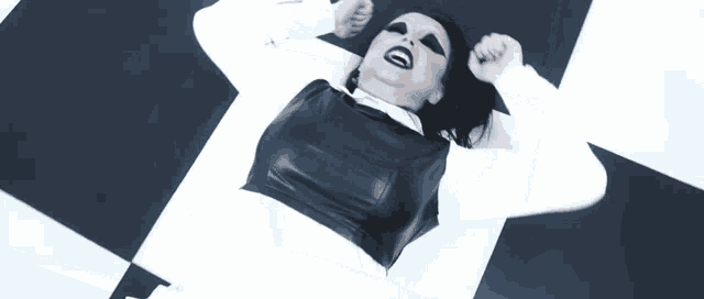 a woman in a black and white outfit is laying on a checkerboard floor