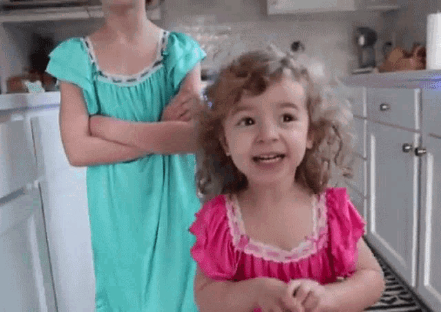 two little girls are standing next to each other in a kitchen .