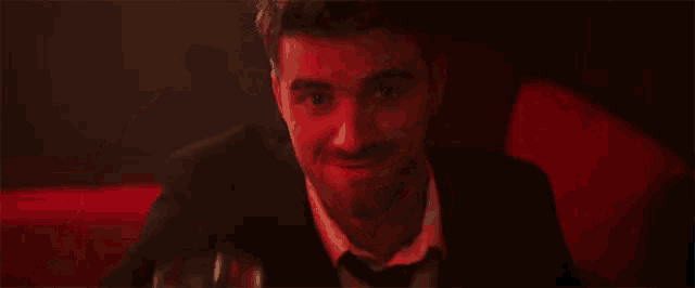a man in a suit and bow tie is pointing at the camera in a red room