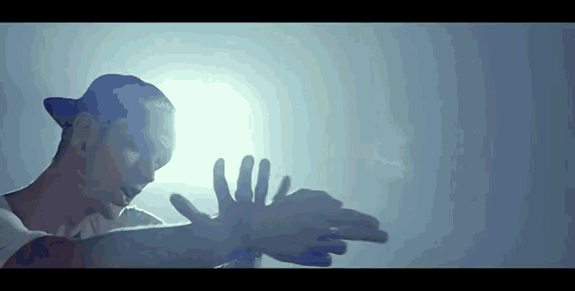 a man wearing a hat and a white shirt is making a hand gesture with his hands