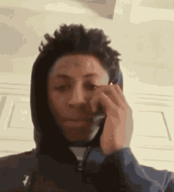 a young man is talking on a cell phone while wearing a hoodie .