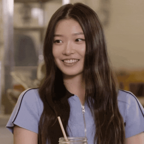 a woman in a blue shirt is smiling and holding a straw