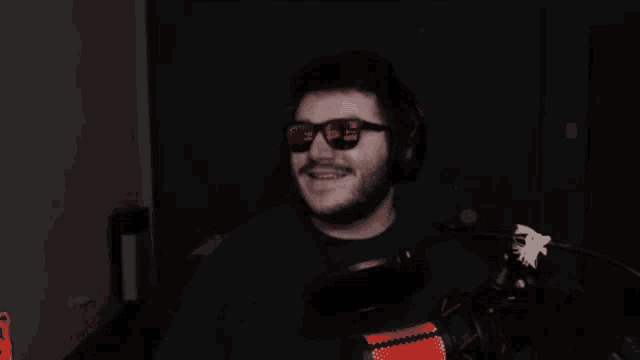 a man wearing headphones and sunglasses is standing in front of a microphone .