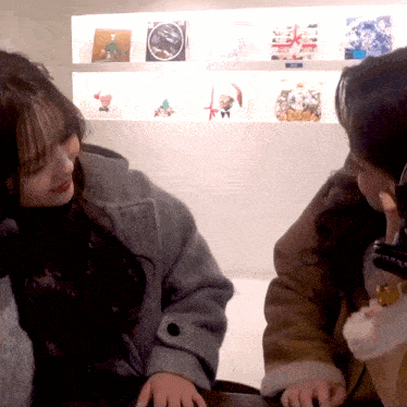 two women are sitting in front of a wall with pictures on it and a sign that says ' christmas ' on it