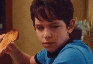 a young boy in a blue shirt is eating a piece of pizza .