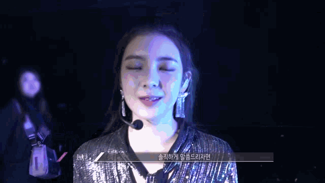 a woman wearing a black sequined top and earrings looks at the camera