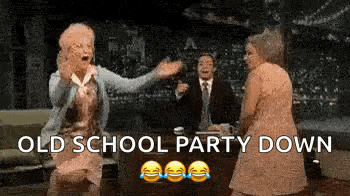 two older women are dancing in front of a man in a suit on a show .