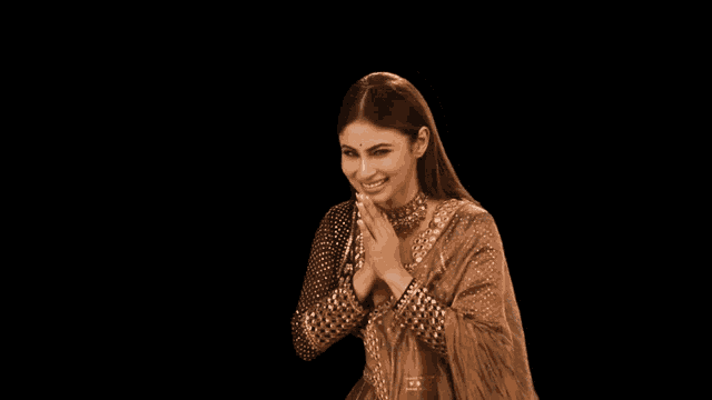 a woman in a brown dress is smiling with her hands folded in front of her face
