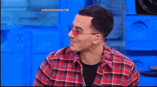 a man wearing sunglasses and a plaid shirt is sitting in front of a blue wall
