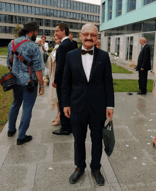 a man in a tuxedo and bow tie is standing in front of a building