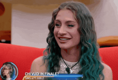 a woman with blue hair is sitting on a red couch and smiling