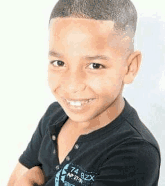 a young boy with a shaved head is smiling for the camera while wearing a black shirt .