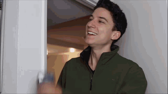 a young man in a green jacket is standing in a doorway and smiling .