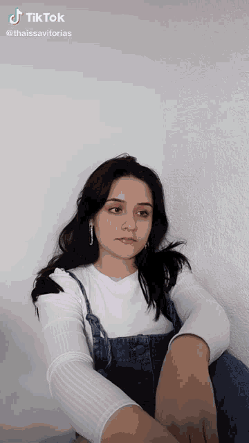 a woman is sitting in front of a wall with a tiktok watermark on the bottom