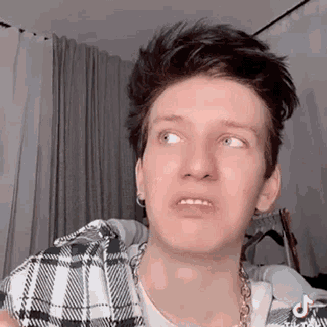 a young man is making a funny face while holding a plaid shirt and a necklace .