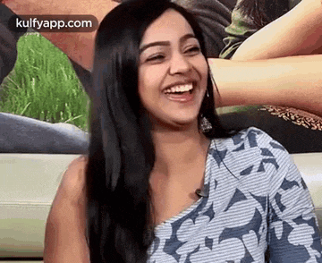 a woman is laughing while sitting on a couch in front of a picture of a man .