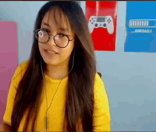a girl wearing glasses and a yellow shirt is sitting in front of a video game controller .