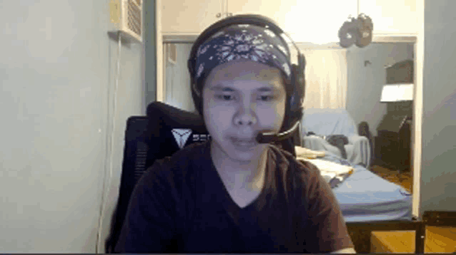 a man wearing headphones and a bandana looks at the camera in a living room