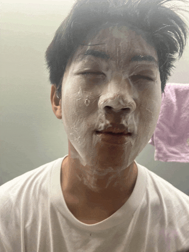 a young man is washing his face with a purple towel behind him