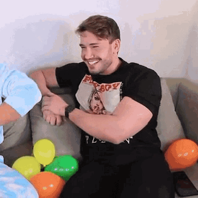 a man wearing a black shirt that says privacy is sitting on a couch with balloons around him