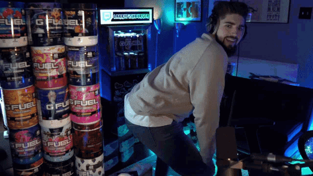 a man wearing headphones stands in front of a stack of g fuel cans