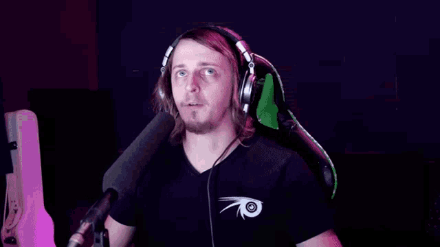 a man wearing headphones and a black shirt is sitting in front of a microphone with his arms outstretched .