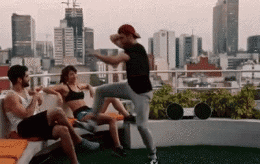 a group of people are dancing on a rooftop with a city in the background ..
