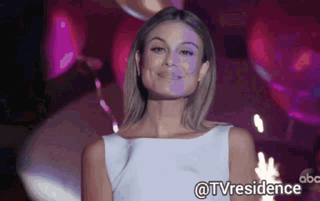 a woman in a white dress is standing in front of balloons and a sign that says tv residence .
