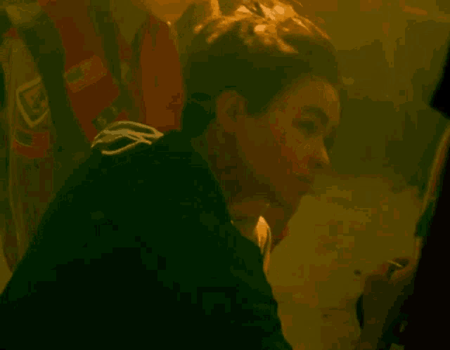 a young man in a black jacket is sitting in a dark room looking at the camera .