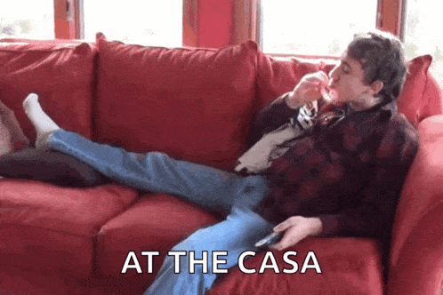 a man is laying on a red couch with the words at the casa written above him