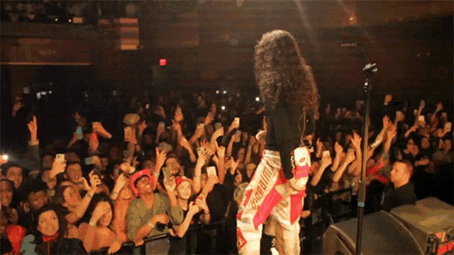 a woman singing into a microphone in front of a crowd that is holding their cell phones