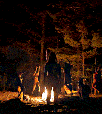 a naked woman stands in front of a fire in the woods