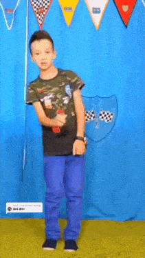 a man in a colorful shirt and jeans is standing in front of a blue wall .